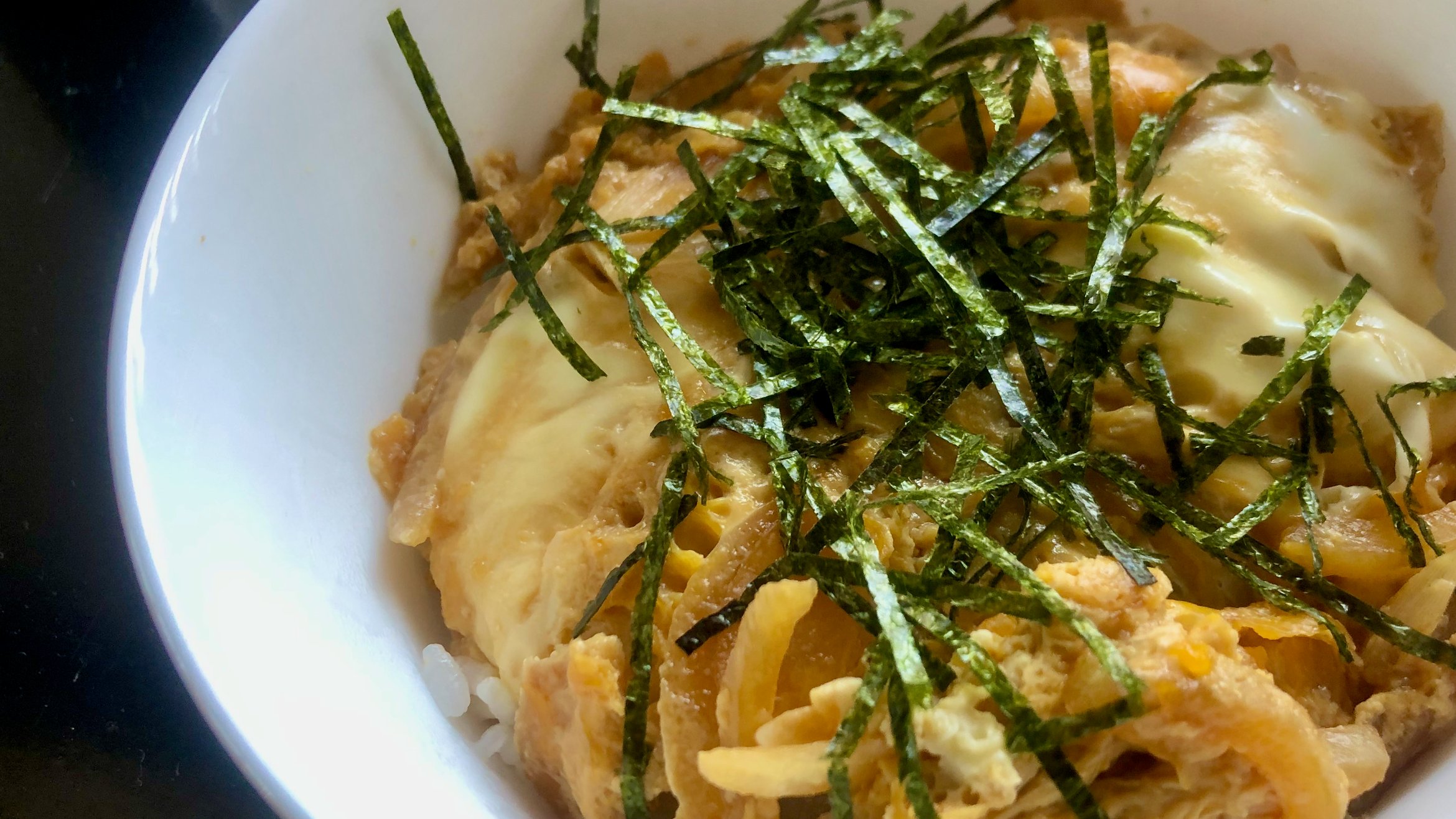 Cover Photo: closeup photograph of kodomo-don (egg with onion and  other seasonings over white rice, topped with slivered nori) in a white bowl