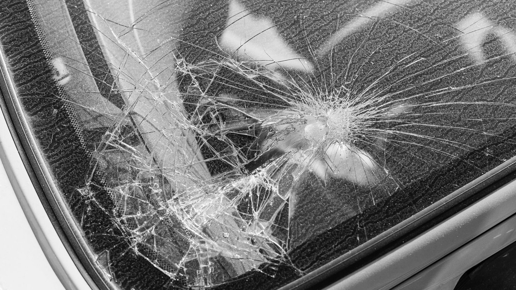 Cover Photo: A close-up black-and-white photo of the shattered window of a car.